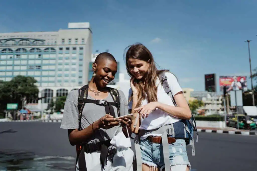 Two female travelers with backpacks looking at a smartphone in an urban setting