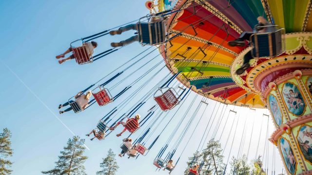 Kouvola, Finland – 18 May 2019: Ride Swing Carousel in motion in amusement park Tykkimaki and aircraft trail in sky. Kouvola, Finland - 18 May 2019: Ride Swing Carousel in motion in amusement park Tykkimaki and aircraft trail in sky.